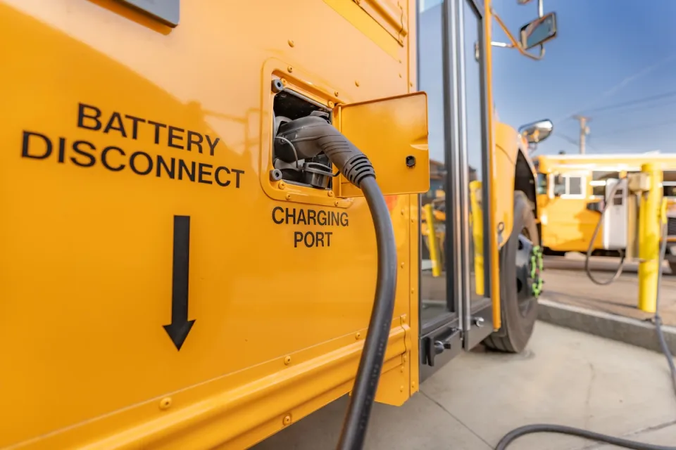 Close-up of charging port on yellow electric school bus plugged in at charging station.
